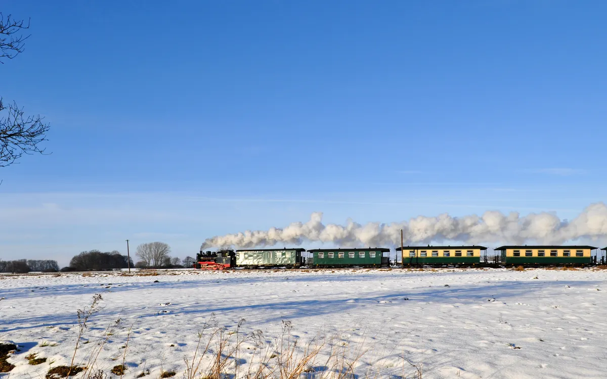 Dampfzug fährt durch verschneite Landschaft unter blauem Himmel