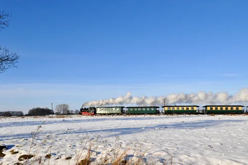 Dampfzug fährt durch verschneite Landschaft unter blauem Himmel