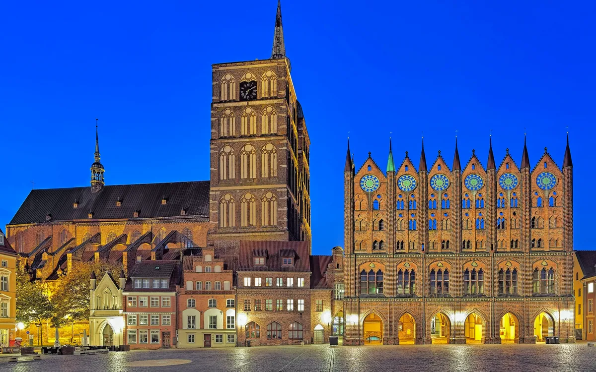 Illuminierte historische Gebäude bei Nacht auf einem Platz vor klarem Himmel.