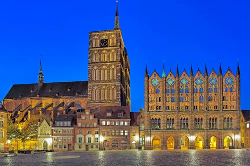 Illuminierte historische Gebäude bei Nacht auf einem Platz vor klarem Himmel.