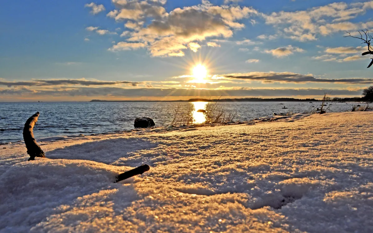 Verschneite Küste bei Sonnenuntergang mit Blick auf das Meer.