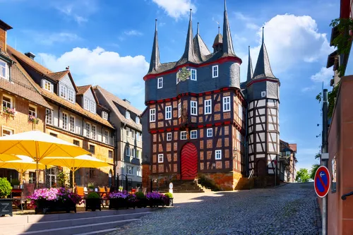 Lebhaftes Fachwerkhaus mit Türmen und sonnigem Marktplatz.
