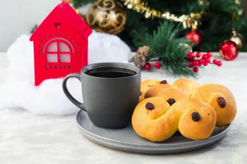 Lussekatter und Tasse Kaffee vor weihnachtlicher Dekoration.