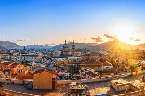 Panorama von Palermo bei Sonnenuntergang mit historischen Gebäuden und Bergen im Hintergrund.