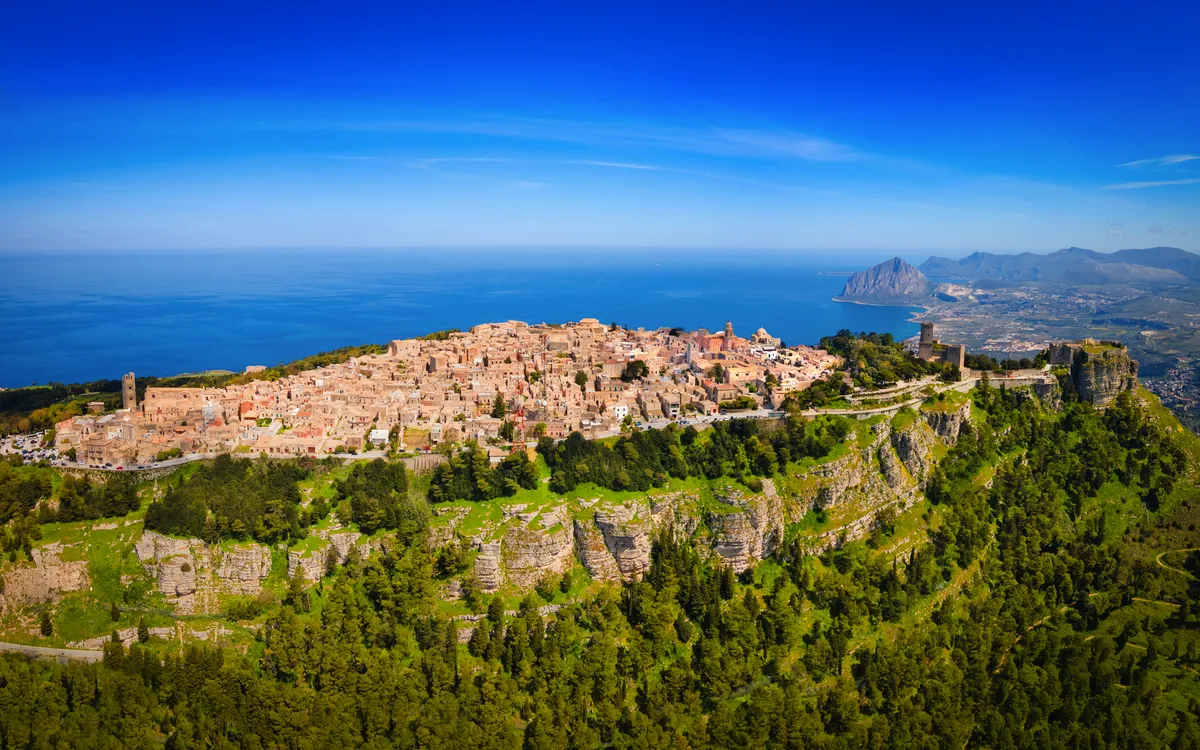 Luftaufnahme einer Stadt auf einem Hügel mit Meer im Hintergrund.