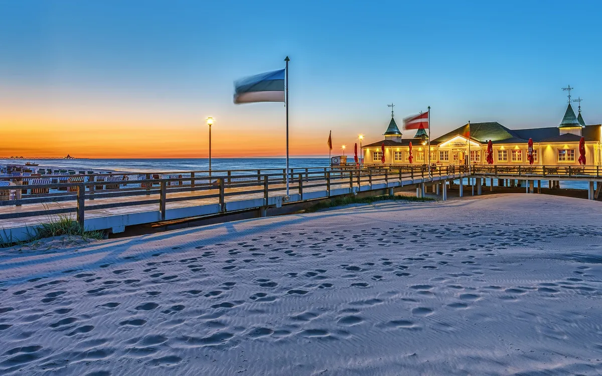 Strandpromenade bei Sonnenuntergang mit Gebäude und Liegestühlen im Sand.