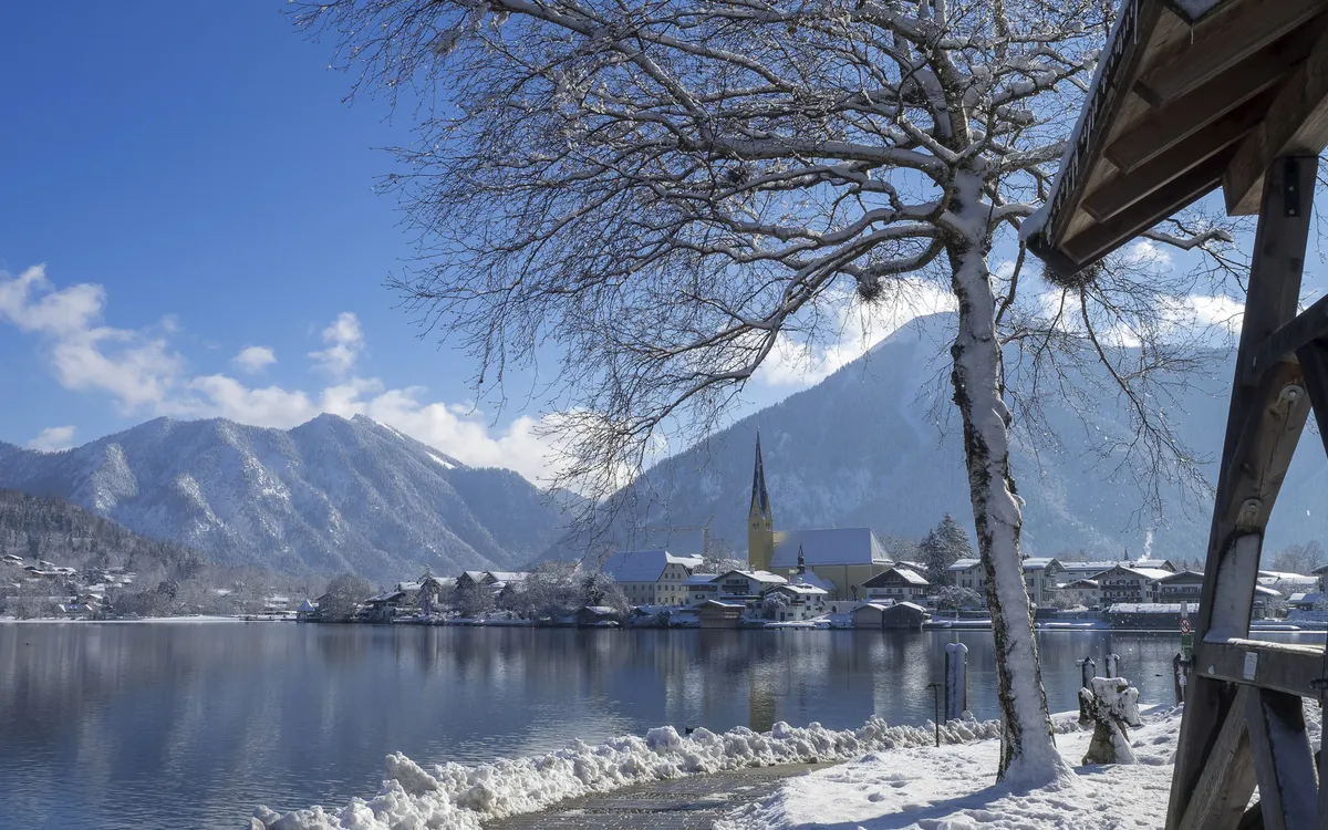 Verschneite Landschaft mit See, Bergen und Dorf im Hintergrund