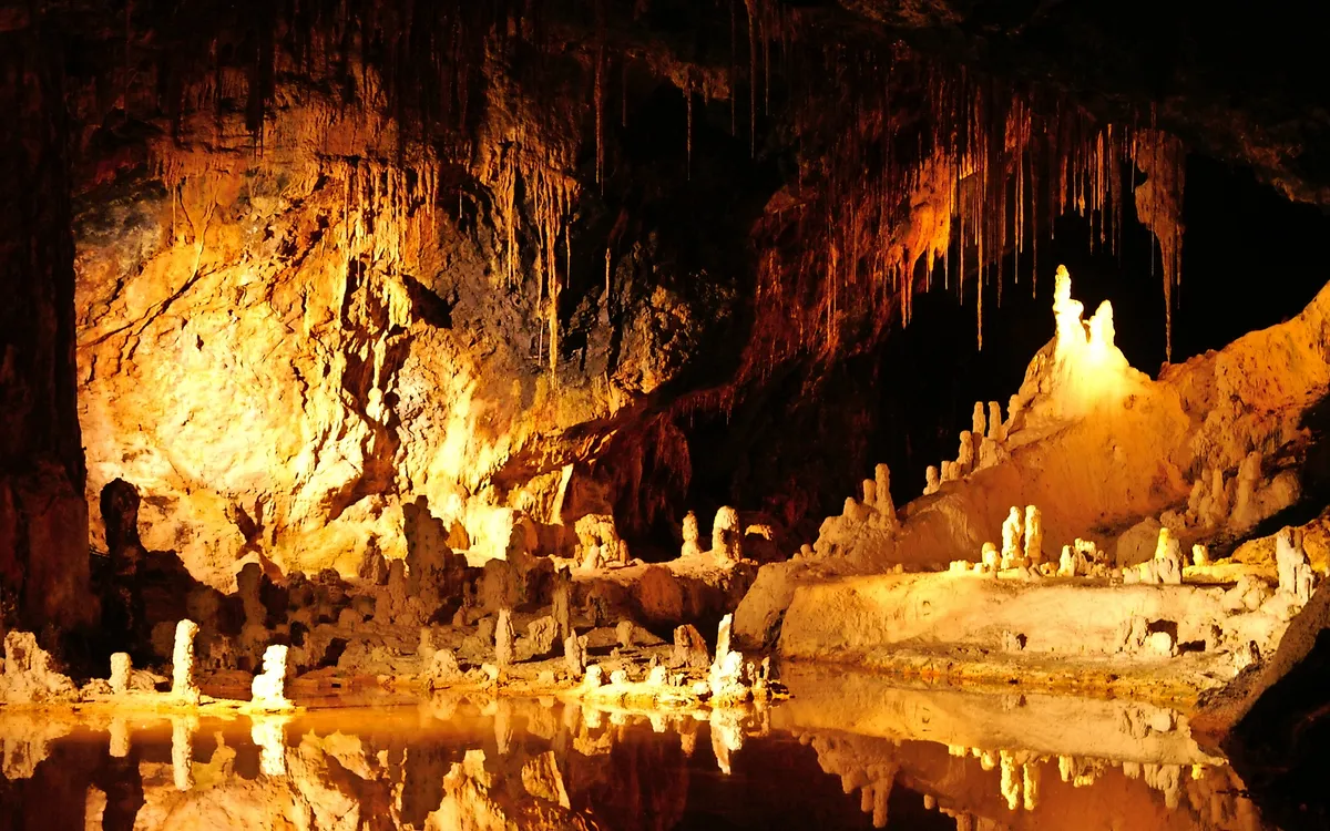Innenansicht einer beleuchteten Höhle mit Stalaktiten und Stalagmiten.
