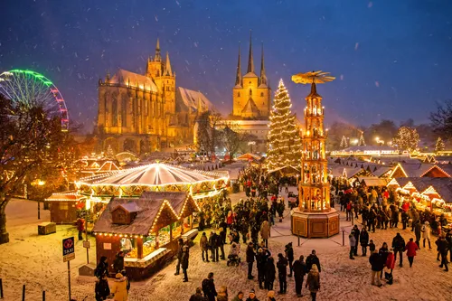 Verschneiter Weihnachtsmarkt mit Lichtern und Menschen in festlicher Stimmung.