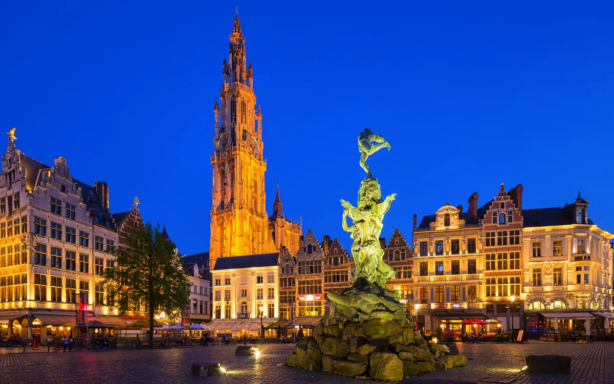 Platz mit Bronzestatue und historischem Glockenturm bei Nacht.