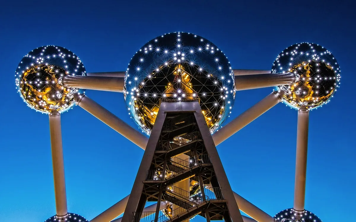 Metallstruktur des Atomiums bei Nacht mit beleuchteten Kugeln und blauem Himmel.