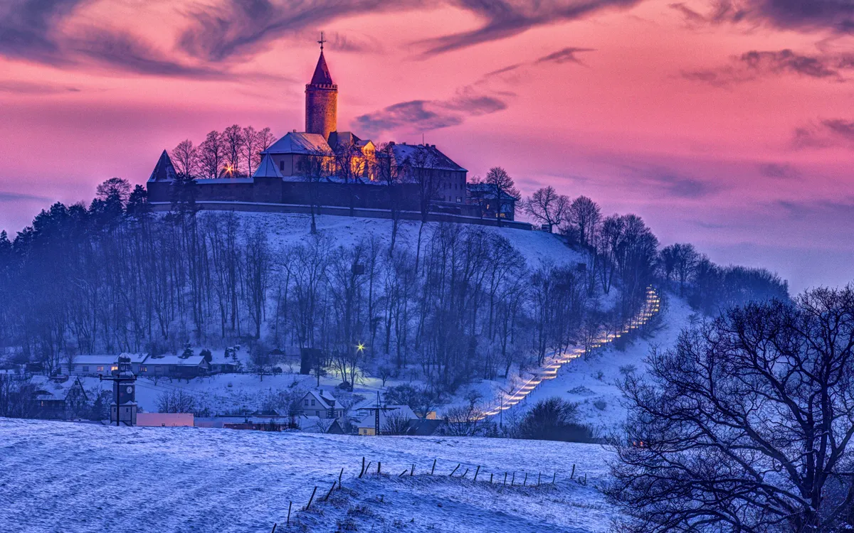Eine beleuchtete Burg auf einem Hügel bei Sonnenuntergang im Winter.