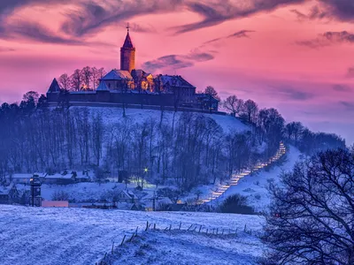 Eine beleuchtete Burg auf einem Hügel bei Sonnenuntergang im Winter.
