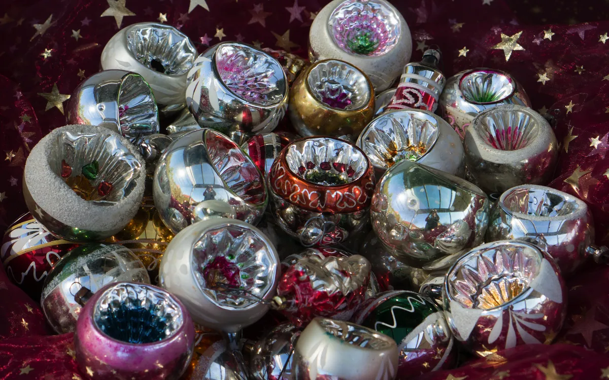 Viele bunte, glänzende Weihnachtskugeln auf rotem Stoff mit goldenen Sternen.