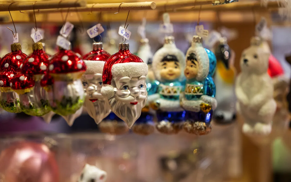 Weihnachtliche Glasdekorationen mit Figuren und Ornamenten hängen auf einem Weihnachtsmarkt.