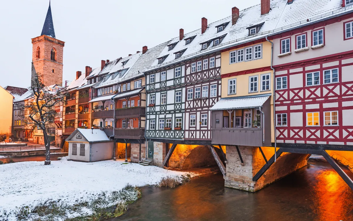 Mehrstöckige Fachwerkhäuser überbrücken im Winter ein kleines Gewässer.