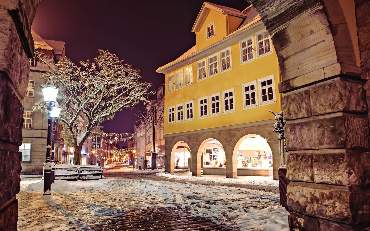 Verschneite Altstadt bei Nacht, beleuchtet mit Laternen.