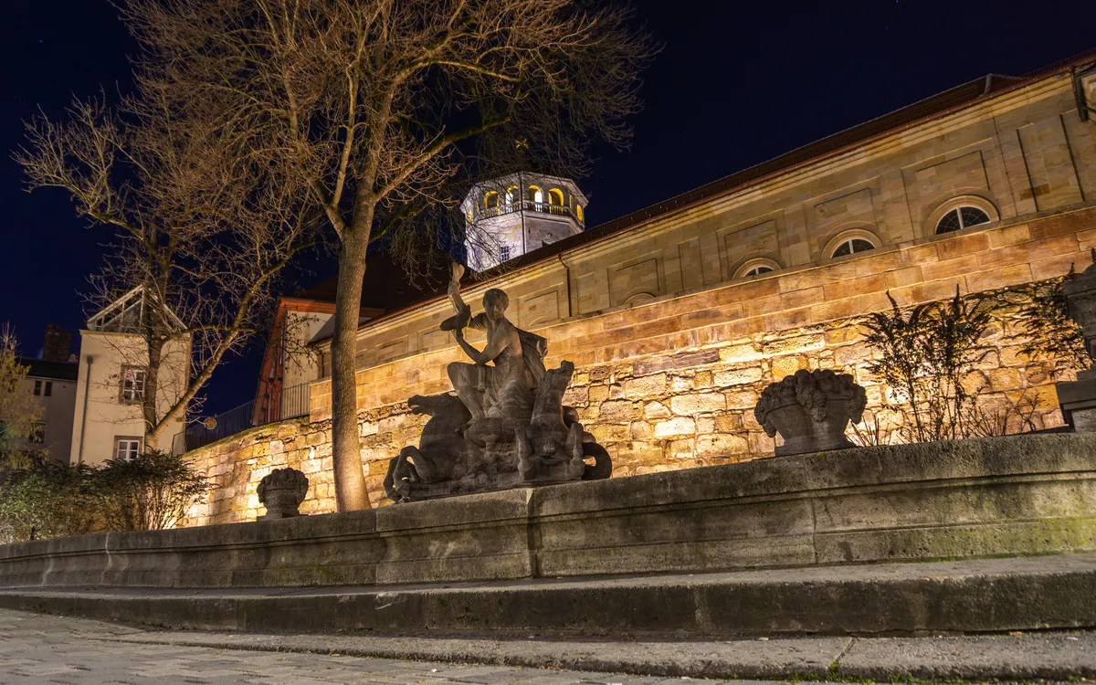 Statue beim Brunnen gegenüber dem Markgräflichen Opernhaus in Bayreuth bei Nacht im Winter.