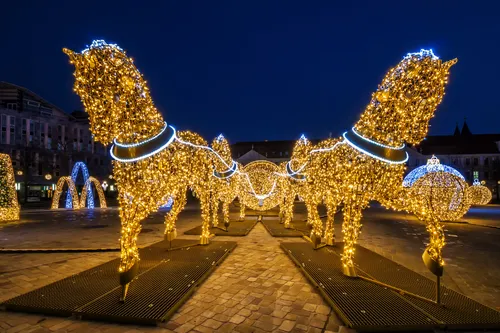 Leuchtende Pferdeskulpturen aus Lichtern auf einem öffentlichen Platz bei Nacht.
