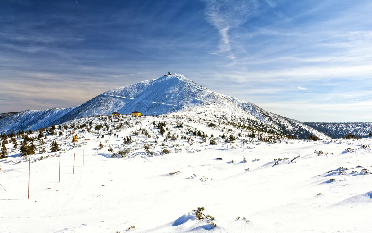 Eine verschneite Berglandschaft unter klarem blauem Himmel mit einem hohen Berg im Hintergrund.