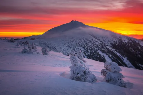 Winterlandschaft mit schneebedecktem Berg bei Sonnenuntergang.