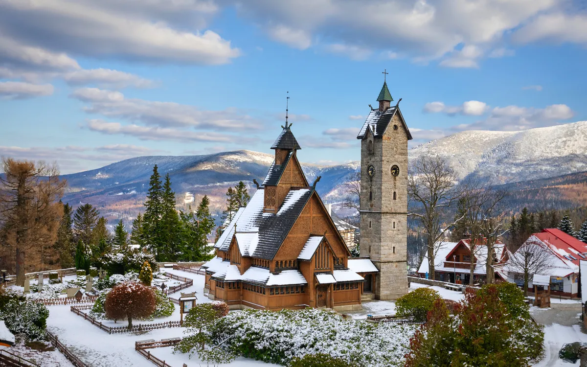 Holzkirche im Schnee mit Bergen im Hintergrund.