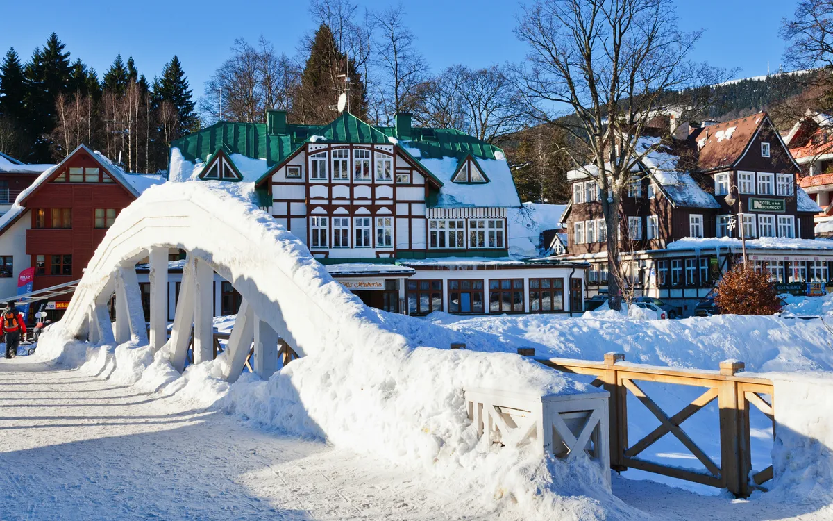 Schneebedeckte Fußgängerbrücke vor Fachwerkhäusern in winterlicher Landschaft.