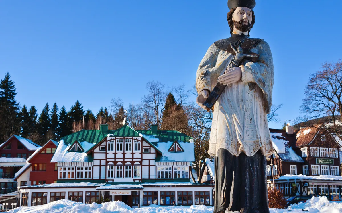Statue vor schneebedeckten traditionellen Häusern und Bäumen im Winter.