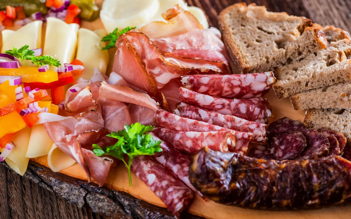 Wurst- und Käseplatte mit Brot auf einem Holzbrett serviert.