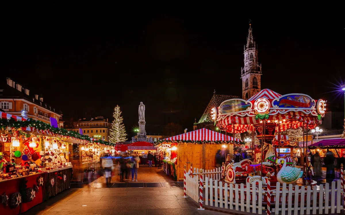 Weihnachtsmarkt bei Nacht mit Karussell und beleuchtetem Baum.