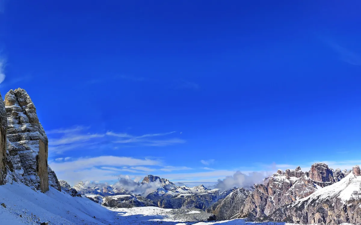 Schneebedecktes Bergpanorama mit klarblauem Himmel, im Vordergrund markante Felsformationen.