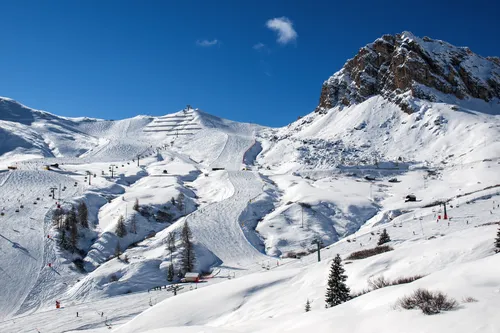 Schneebedeckte Berglandschaft mit Skiliften und Skifahrern, umgeben von blauem Himmel.