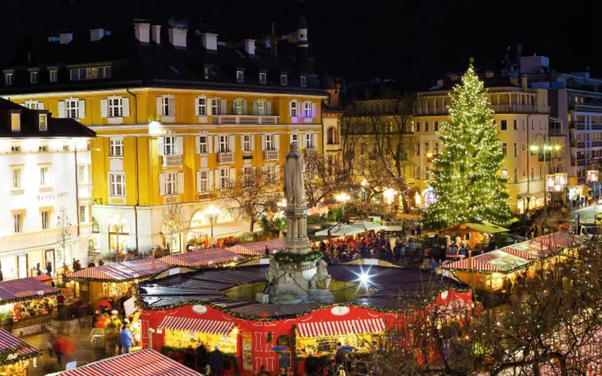 Weihnachtsmarkt mit geschmücktem Baum und Buden bei Nacht