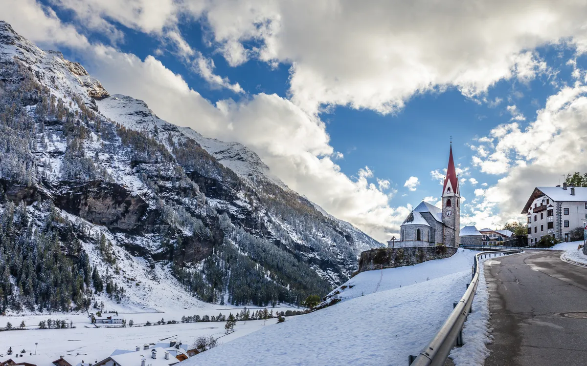 Verschneite Berglandschaft mit Kirche und Dorf unter blauem Himmel.