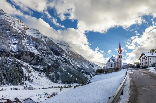 Verschneite Berglandschaft mit Kirche und Dorf unter blauem Himmel.