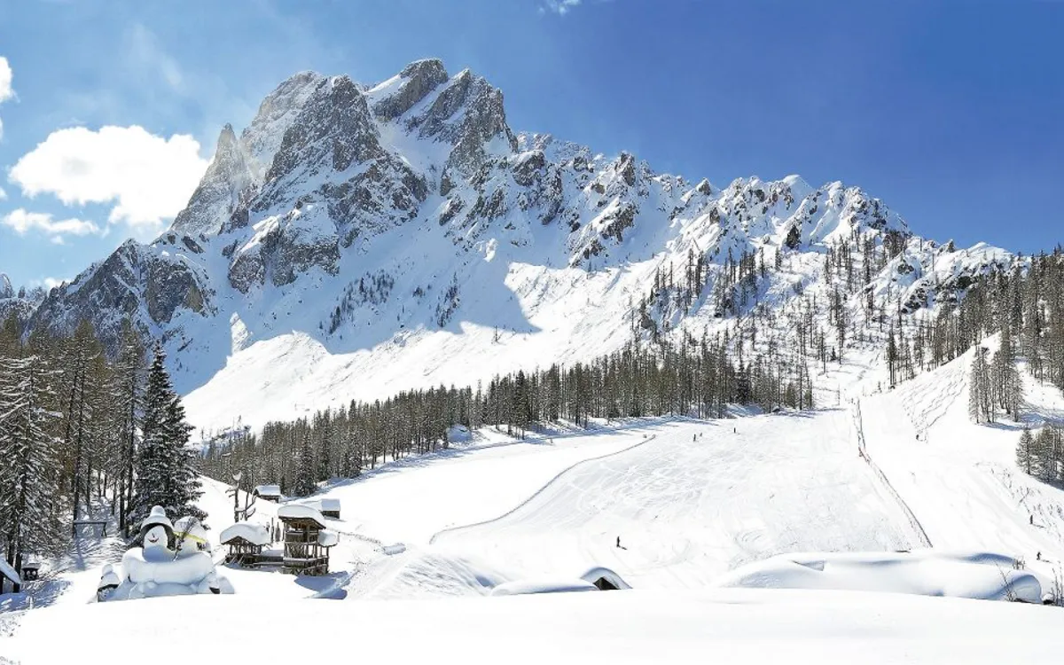 Verschneite Berglandschaft mit Skipiste und bewaldeten Hängen.