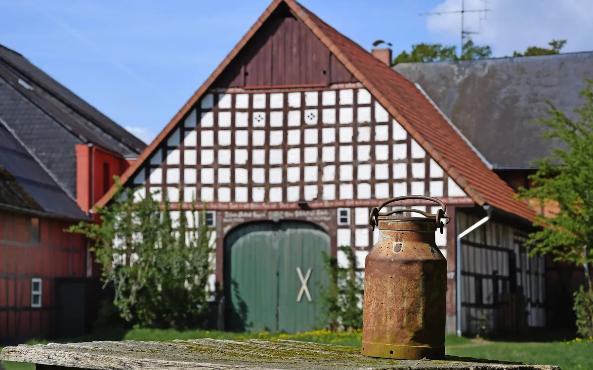 Alte Milchkanne auf einem Tisch mit Fachwerkhaus im Hintergrund im Rundlingsdorf Satemin.