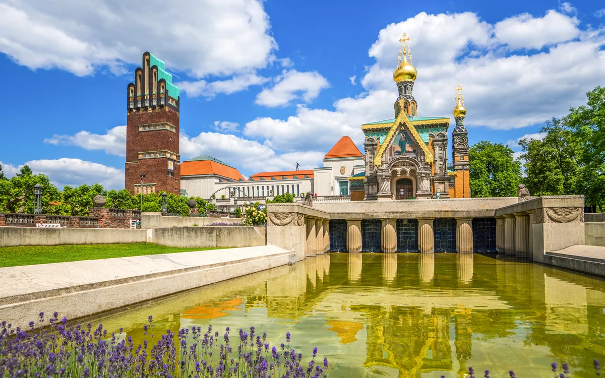 Historischer Gebäudekomplex mit Teich und blühendem Lavendel im Vordergrund.