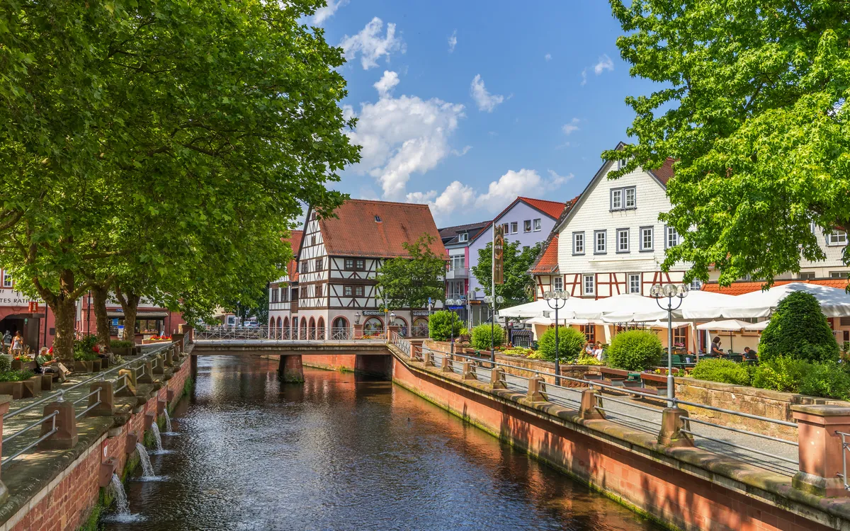 Kanal mit Fachwerkhäusern und Bäumen unter blauem Himmel in deutscher Altstadt.