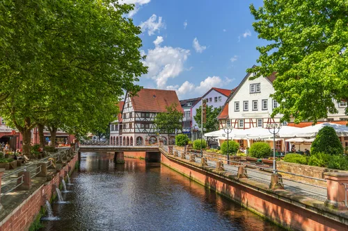 Kanal mit Fachwerkhäusern und Bäumen unter blauem Himmel in deutscher Altstadt.