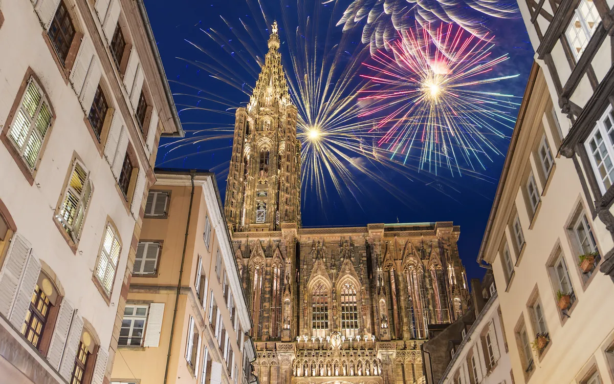 Feuerwerk über der Kathedrale in Straßburg, umgeben von alten Fachwerkhäusern bei Nacht.