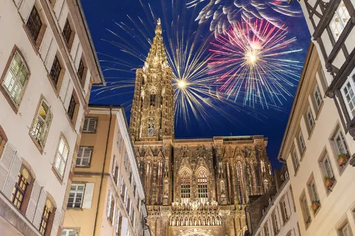 Feuerwerk über der Kathedrale in Straßburg, umgeben von alten Fachwerkhäusern bei Nacht.