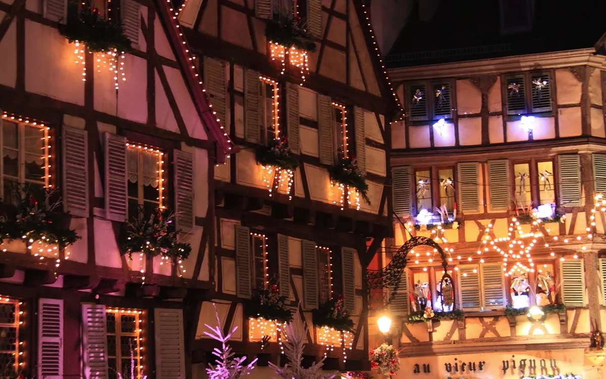 Fachwerkhäuser mit Weihnachtsbeleuchtung in einer abendlichen Straßenszene.