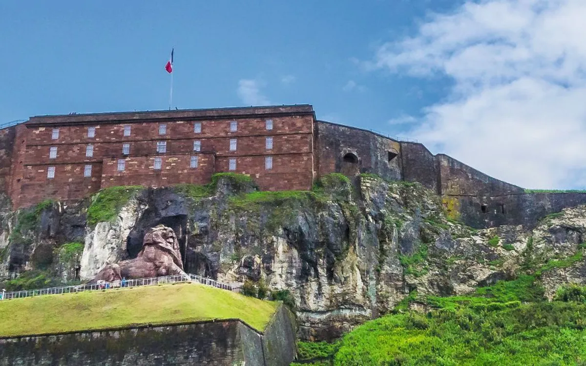 Fort auf einem Hügel mit einem steinernen Löwen darunter, blaue Himmel im Hintergrund.