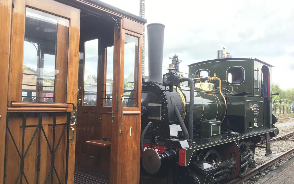Dampflok neben einem historischen Holzwagen auf Gleisen.