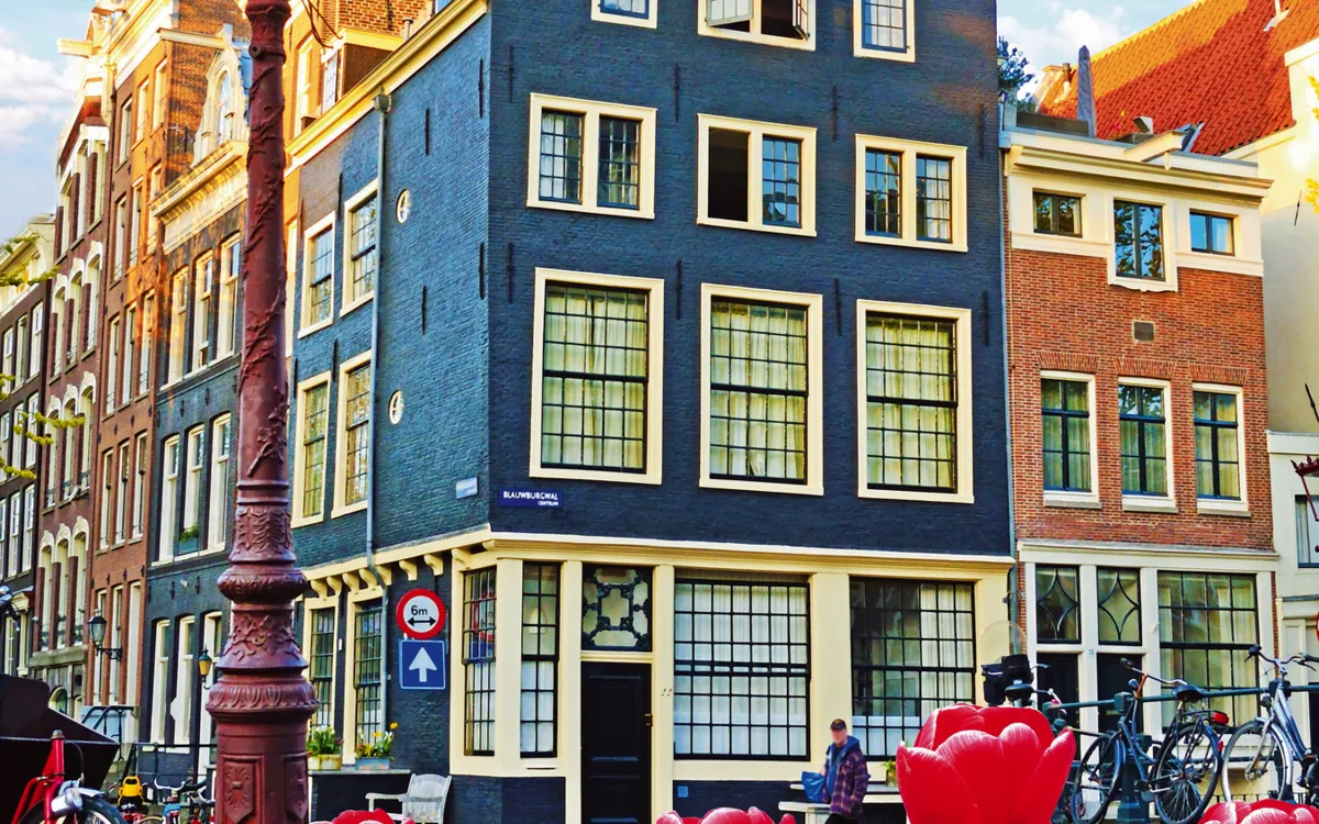 Historische Häuser an einem Amsterdamer Kanal mit Fahrrädern und Blumen im Vordergrund.