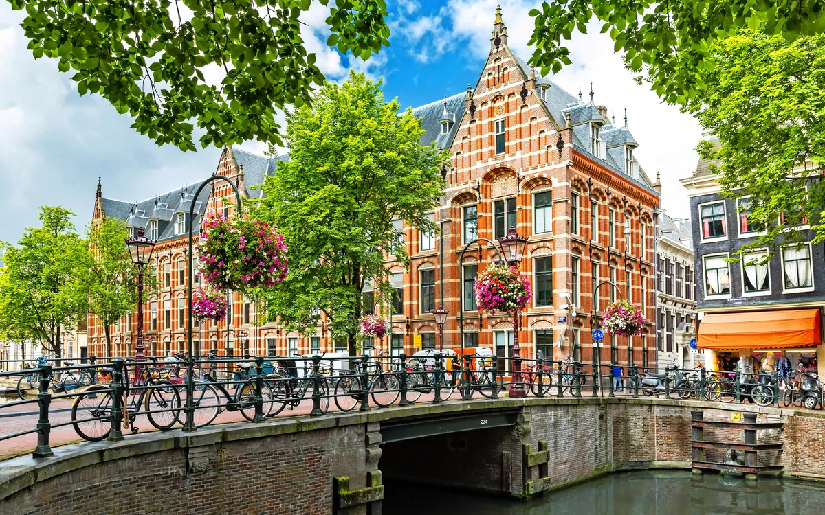 Kanalbrücke in Amsterdam mit traditionellen Häusern und Fahrrädern bei blauem Himmel.