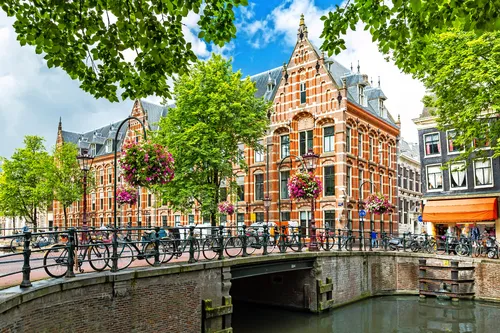 Kanalbrücke in Amsterdam mit traditionellen Häusern und Fahrrädern bei blauem Himmel.