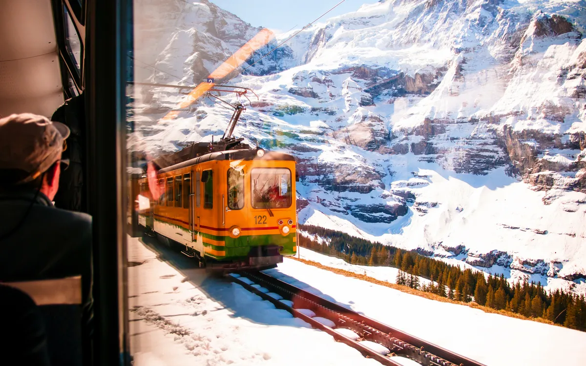 Gelber Zug fährt durch schneebedeckte Berge in der Schweiz.