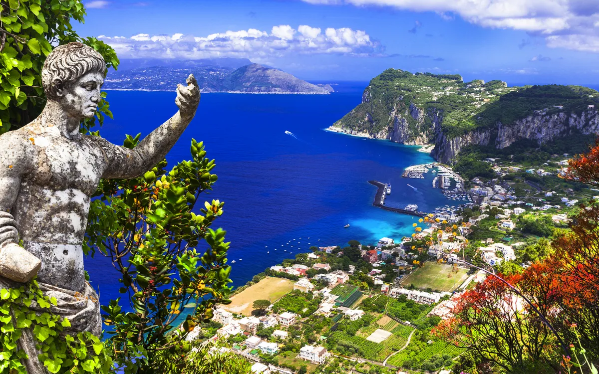 Panorama der Insel Capri mit Statue und Blick auf das blaue Meer und Steilhänge.